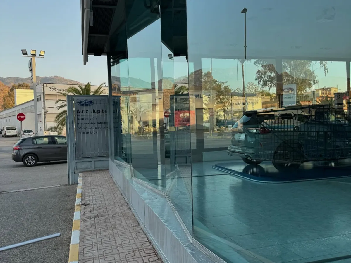 Cristalera de una exposición de coches, recién limpiada, con el reflejo de la calle
